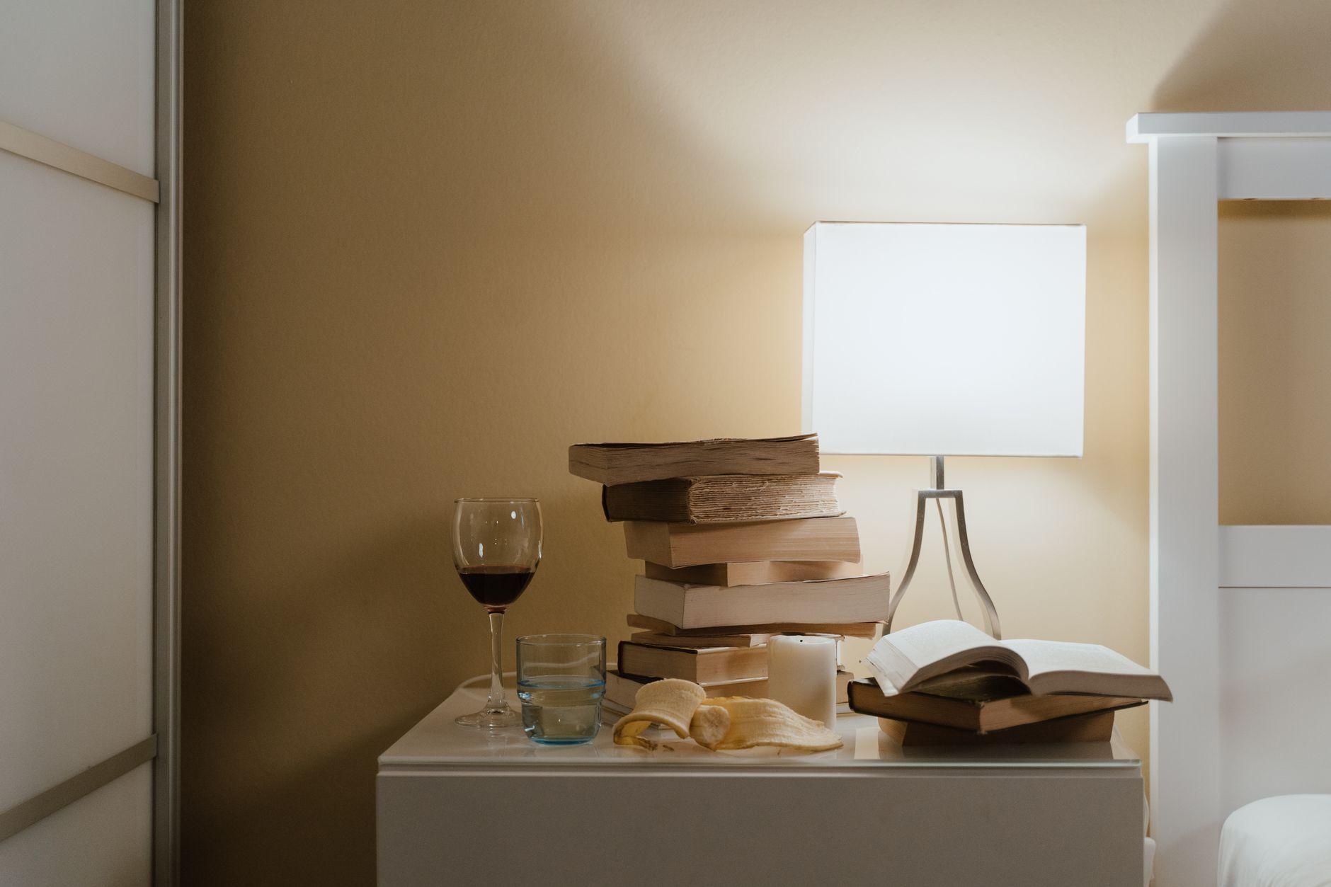 A tall, slightly leaning stack of unread paperback books on a bedside table